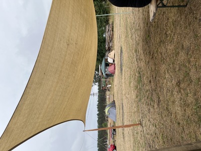 Das Tarp diente als Sonnen- und Regenschutz. Hier wurden die Workshops angehalten. Im Hintergrund sind einige Zelte zu sehen. Der Grasboden ist aufgrund der Trockenheit bräunlich.