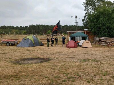 Einige Zelte sind aufgebaut. Man sieht eine Flagge mit rotem Stern und Tastatur auf einem Mast, daneben vier Personen.