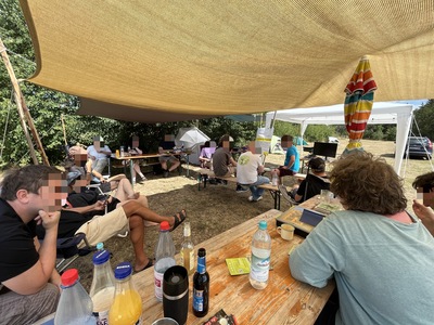 Auch am zweiten Tage gab es Workshops und Vorträge. Hier sitzen die Teilnehmenden auf Bänken unter dem Sonnendach.