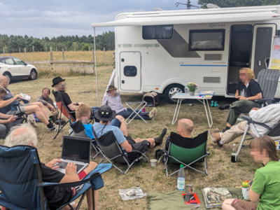 Personen sitzen vor einem Camper im Halbkreis.