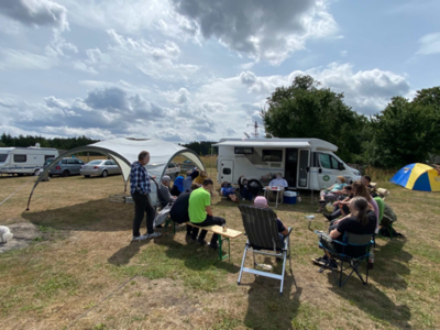 Personen sitzen auf dem Campingplatz und unterhalten sich.