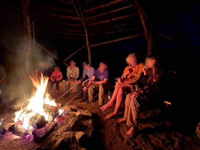 Personen sitzen am Feuer und halten Stöcke mit Marshmallow ins Feuer.