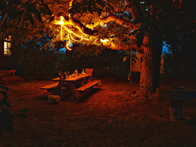 An der Tafel wurden Talks und Workshops abgehalten und zusammen gegessen. Nachts stehen noch Flaschen auf dem Tisch, die von einer Lichterkette im Baum erhellt werden.