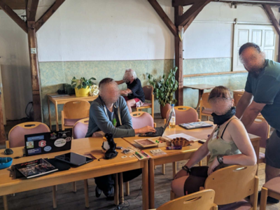 Der Saal bietet viel Platz für Talks und Workshops. Einige Personen sitzen an einem Tisch und schauen in die Kamera.