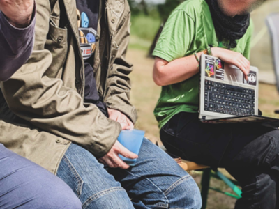 Personen sitzen in der Sonne, eine Person hält einen Laptop in der Hand.