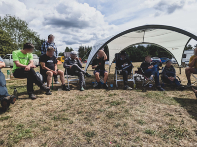 Personen sitzen am Camp, teils unter einem Sonnensegel.