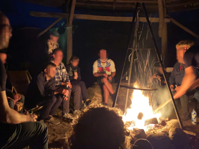 Personen sitzen am Feuer und bereiten ein Dreibein vor.