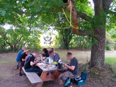 Personen sitzen am Tisch unter einem Baum.