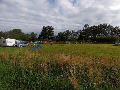 Der Zeltplatz mit Wohnwägen, Zelten und Tarps im Weitwinkel..