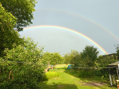 Der Zeltplatz von der Küche aus gesehen. Am Himmel sind Regenbogen zu sehen und die Sonne scheint.