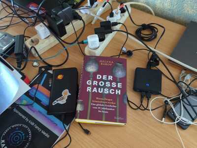 Ladestation für Phones, viele Kabel und ein Buch auf einem Tisch.