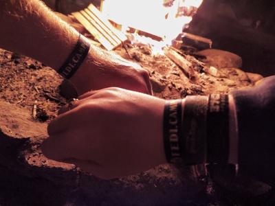 Zwei Hände vor dem Lagerfeuer zeigen das diesjährige FediCamp-Armbändchen.