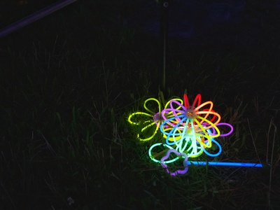 Fluoreszierende Armbänder, Räder und ein Zauberstab leuchten auf der dunklen Wiese in der Nacht.
