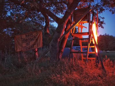 Lichtinstallation und eine Flagge "Kein Mensch ist illegal" bei Nacht.
