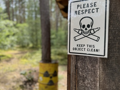 Fässer im Wald als Mahnmal der Atomenergie. Auf einem Schild steht "Keep this object clean".